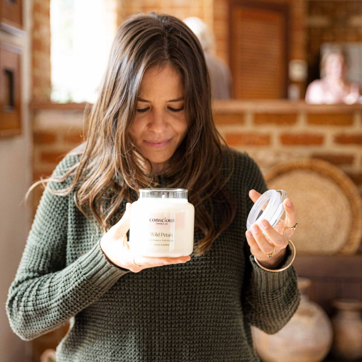 Woman holding two ceramic jars in a home setting with a brick wall background